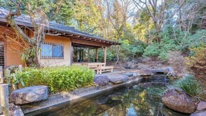 A traditional Japanese-style building with a wooden exterior, a stone pathway, and a small pond with rocks. - KEYAKIZAKA (Ito)