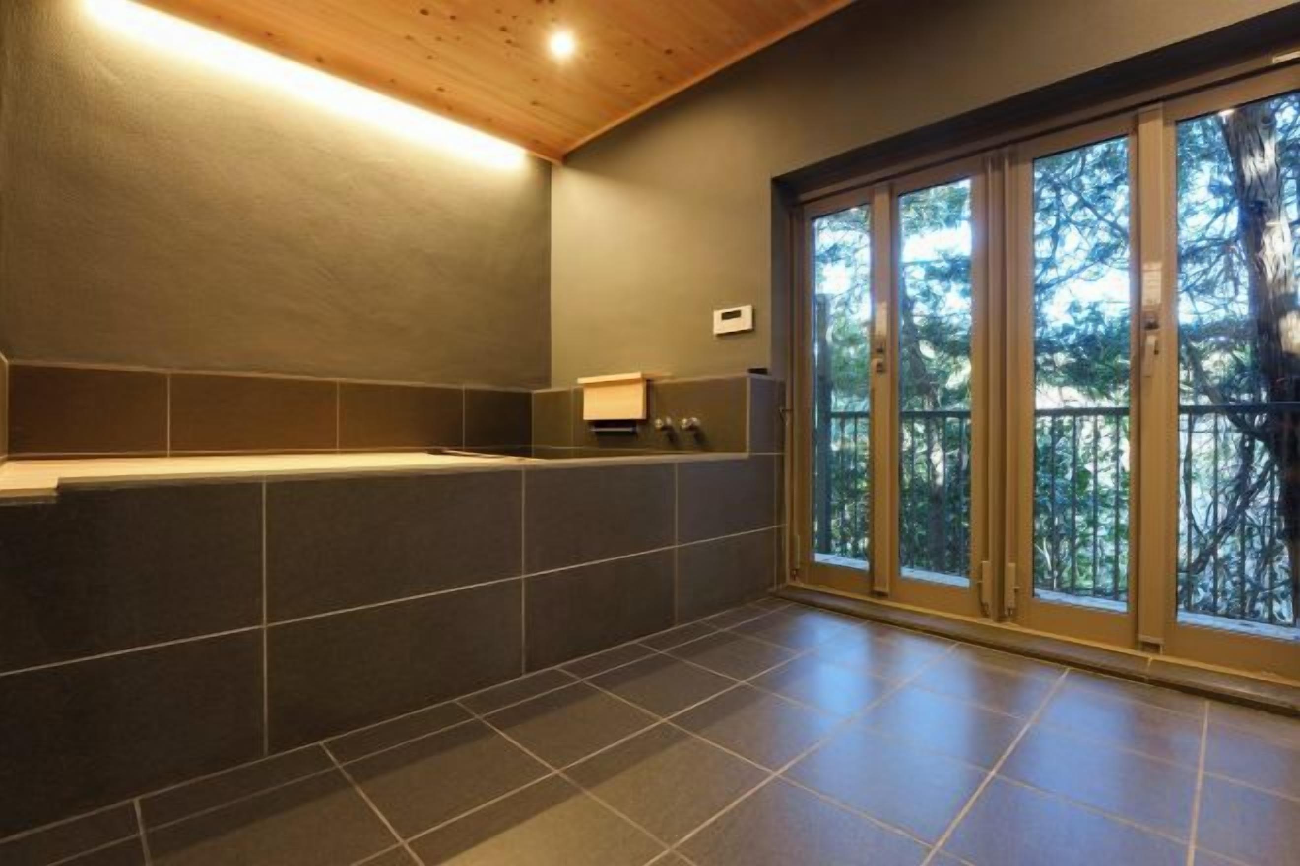 A modern bathroom with a bathtub, large windows, and a view of trees.