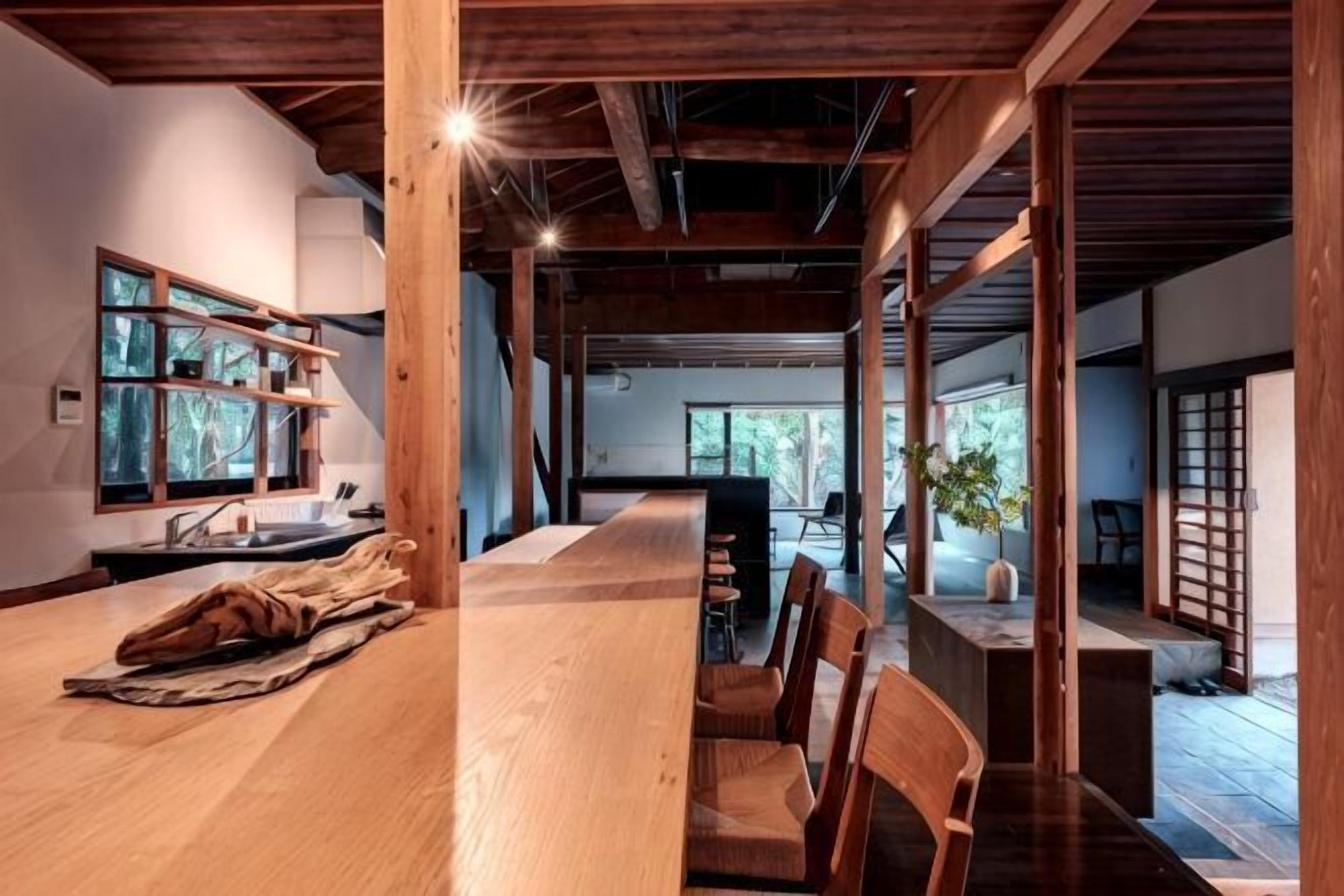 A spacious room with a long wooden table, chairs, a window with shelves, and a view of the outdoors.