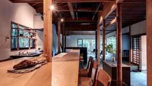 A spacious room with a long wooden table, chairs, a window with shelves, and a view of the outdoors. - KEYAKIZAKA (Ito)