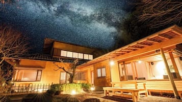 A traditional Japanese house with a wooden exterior, a covered outdoor seating area, and a view of the night sky.