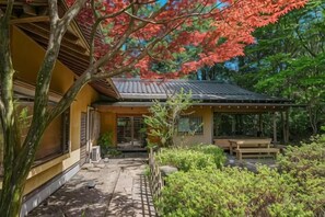 A traditional Japanese building with a covered patio, a wooden bench, and a stone pathway. - KEYAKIZAKA (Ito)