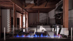 A modern interior with a glass table featuring a blue flame, wooden beams on the ceiling, and a bookshelf on the right. - KEYAKIZAKA (Ito)
