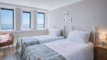 A bedroom with two beds, a window with a view, a chair, and a bedside table with a lamp.