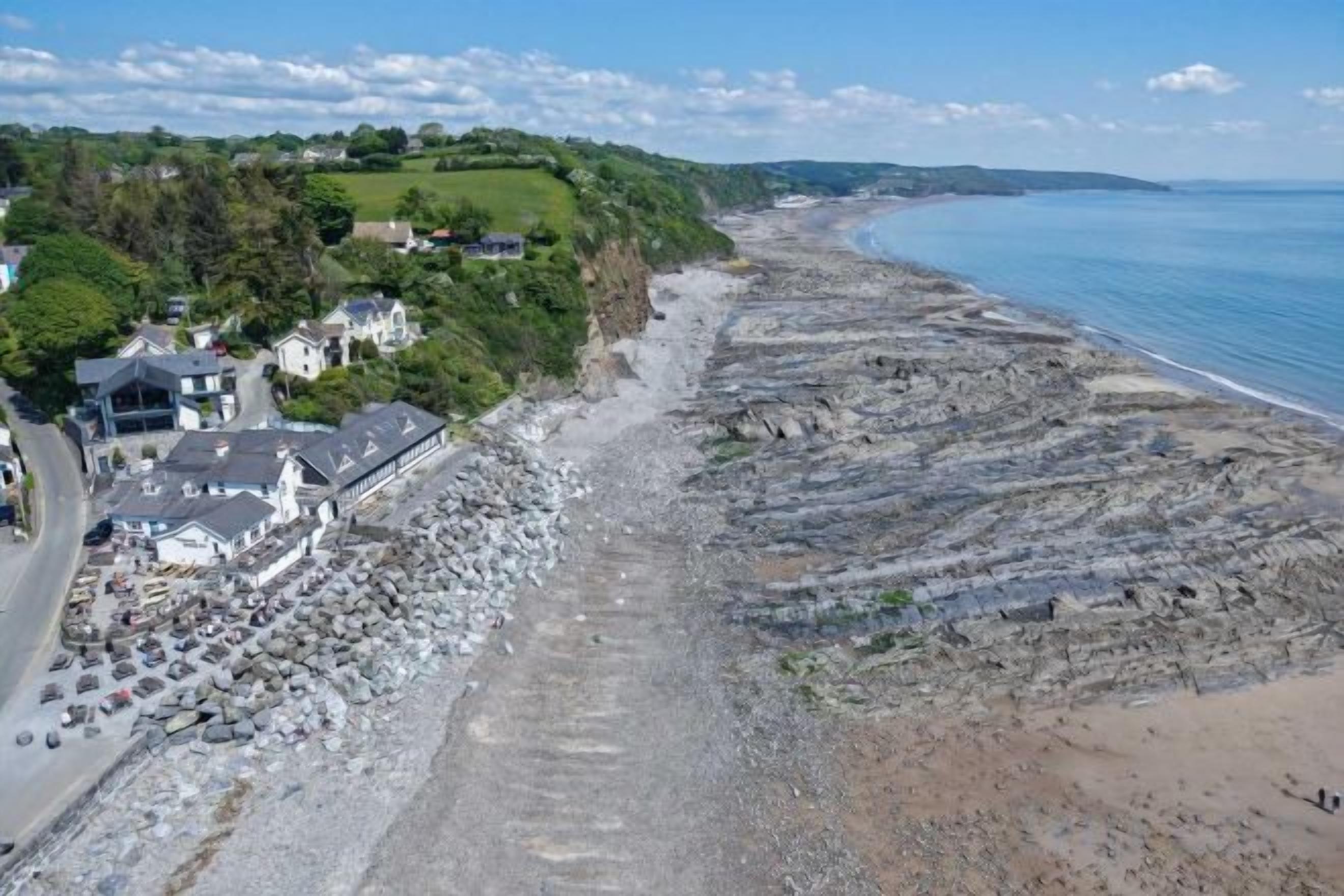 A coastal property with a rocky beach, a road, and a building with multiple rooms.