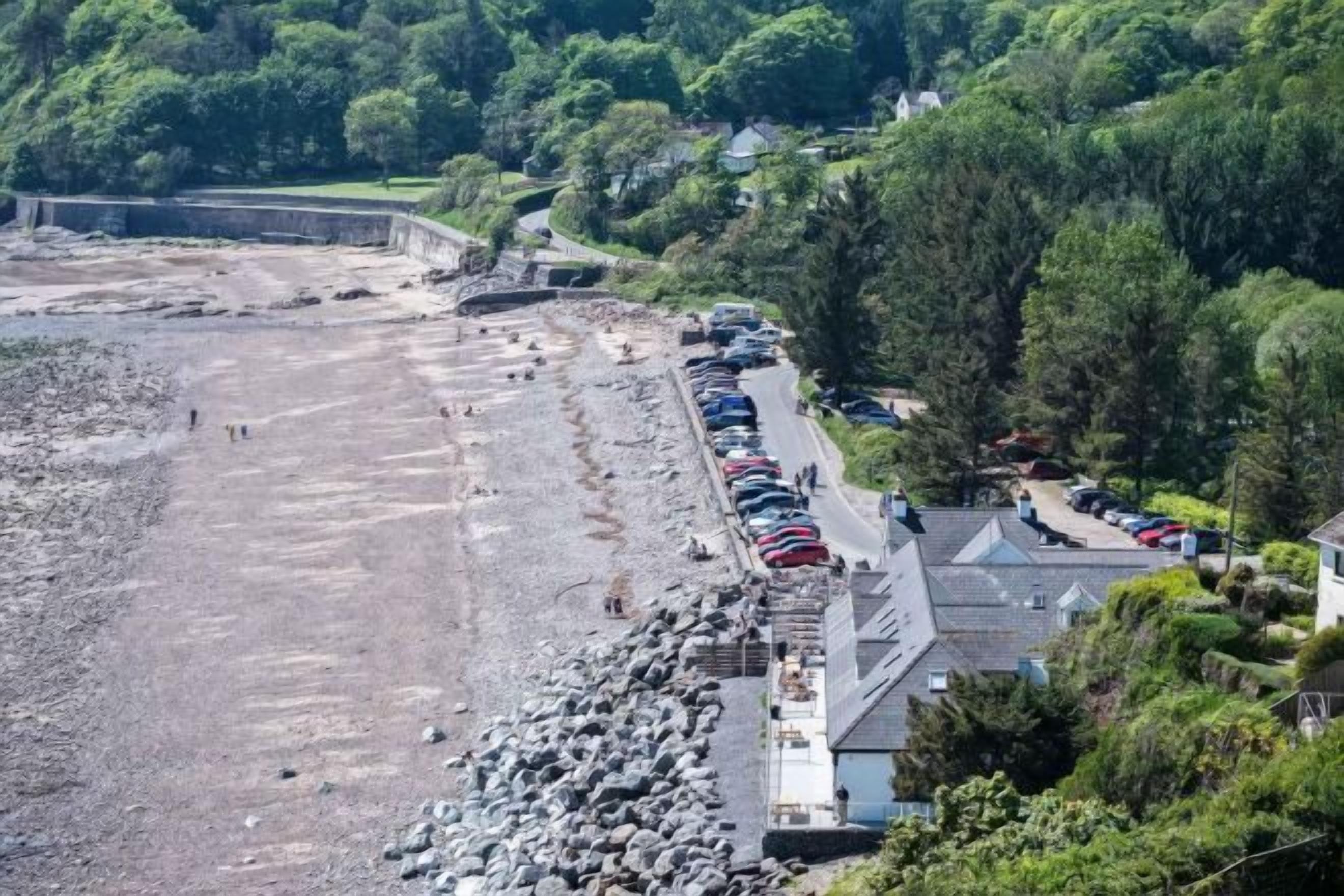 Una zona costera con playa rocosa, coches aparcados y edificios con tejados inclinados.