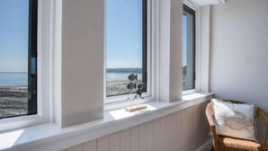 Een kamer met uitzicht op het strand, een rieten stoel en een tafeltje met decoratieve objecten.