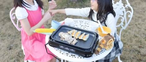 Two individuals seated at a table with a grill containing food.
