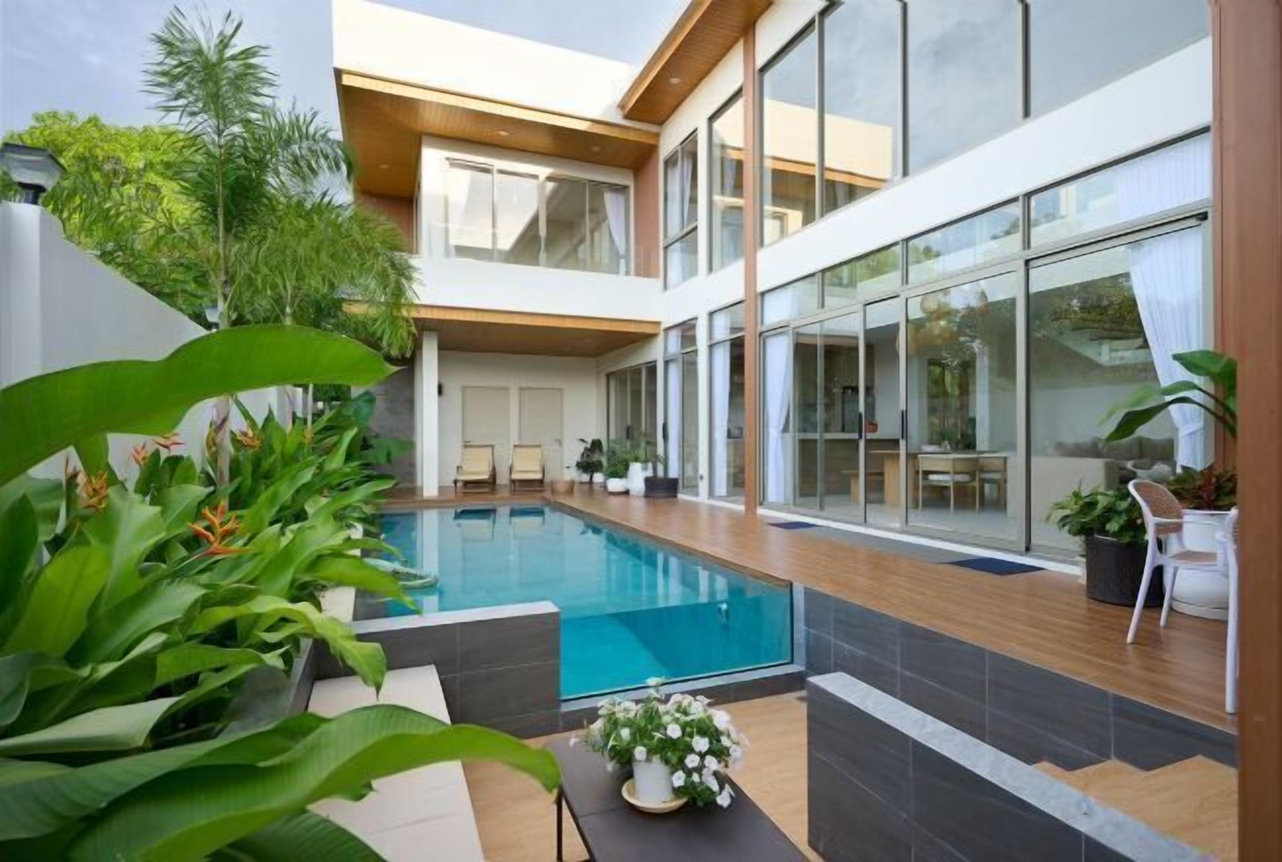 A modern indoor swimming pool with a view of the sky, surrounded by large windows and indoor plants.