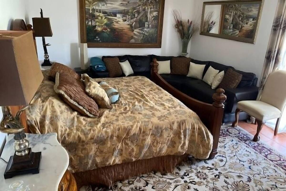 A bedroom with a large bed, a sofa, a chair, and two paintings on the wall.