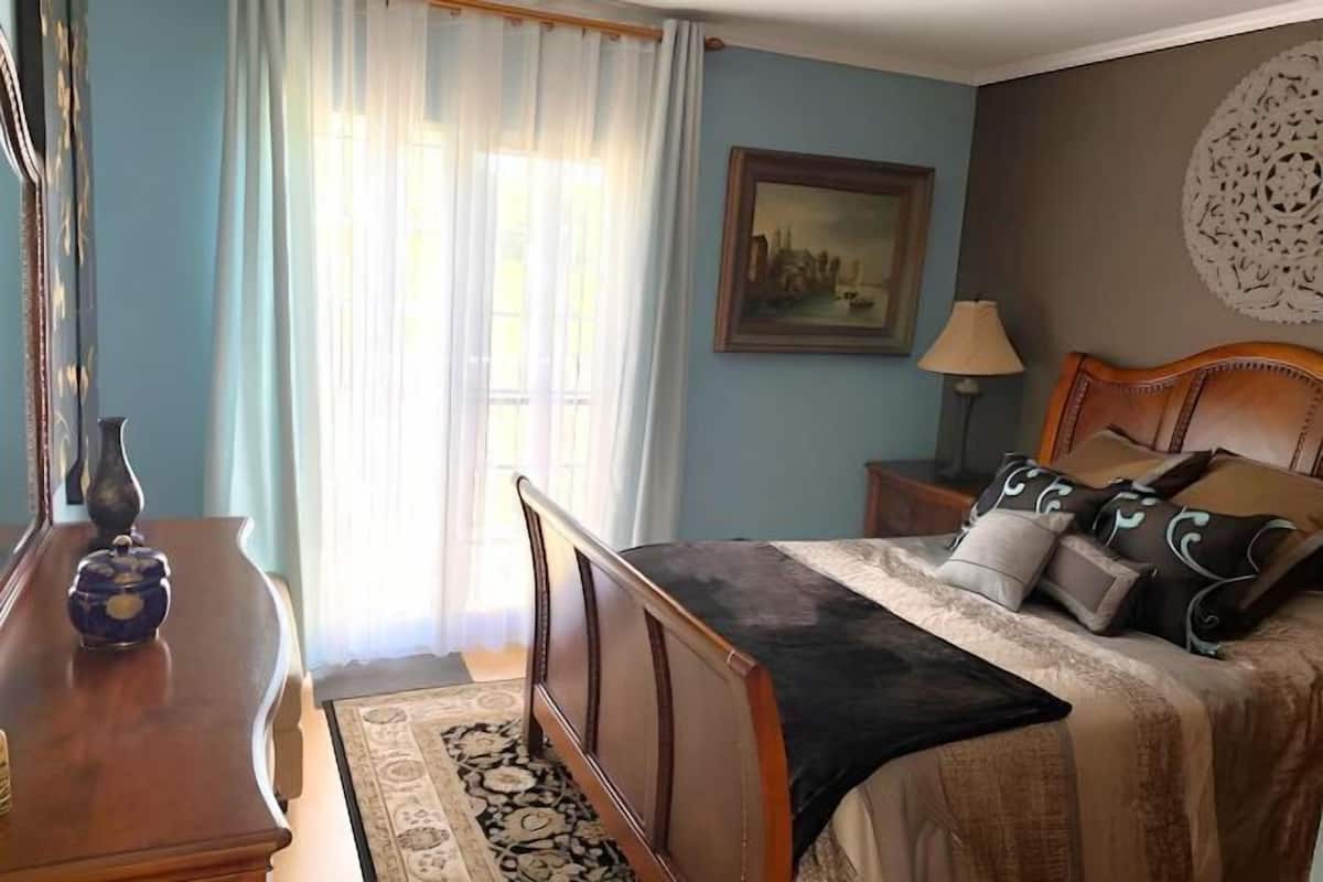 A bedroom with a bed, a nightstand, a lamp, a dresser, and a window with curtains.