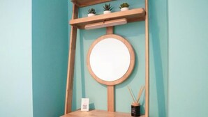 Een houten wastafel met een ronde spiegel, een klein plankje met potplanten, en een lade met een kaars en rietverspreider.