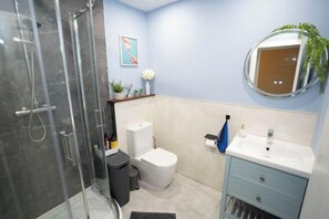 Ein Badezimmer mit Duschkabine aus Glas, Toilette, Waschbecken mit Spiegel und einem blauen Schrank.