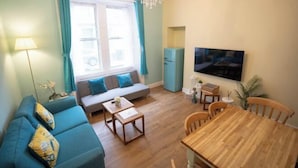 Een woonkamer met een bank, een eettafel, een televisie en een koelkast.