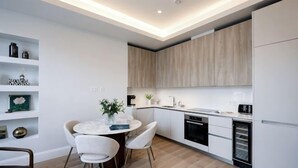 A modern kitchen with white cabinetry, a dining table with chairs, and a built-in oven. - 311 Superior Maisonette (London)