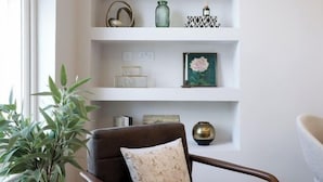 A living room with a brown leather armchair, a white sofa, and a white shelving unit with decorative items. - 311 Superior Maisonette (London)