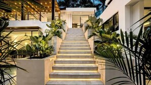 A modern staircase with illuminated steps, flanked by large planters with tropical plants, leading to a building entrance. - Villa Oasis by BaliSuperHost (Bali)