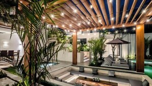 A modern outdoor lounge area with a wooden pergola, seating, and a small water feature. - Villa Oasis by BaliSuperHost (Bali)