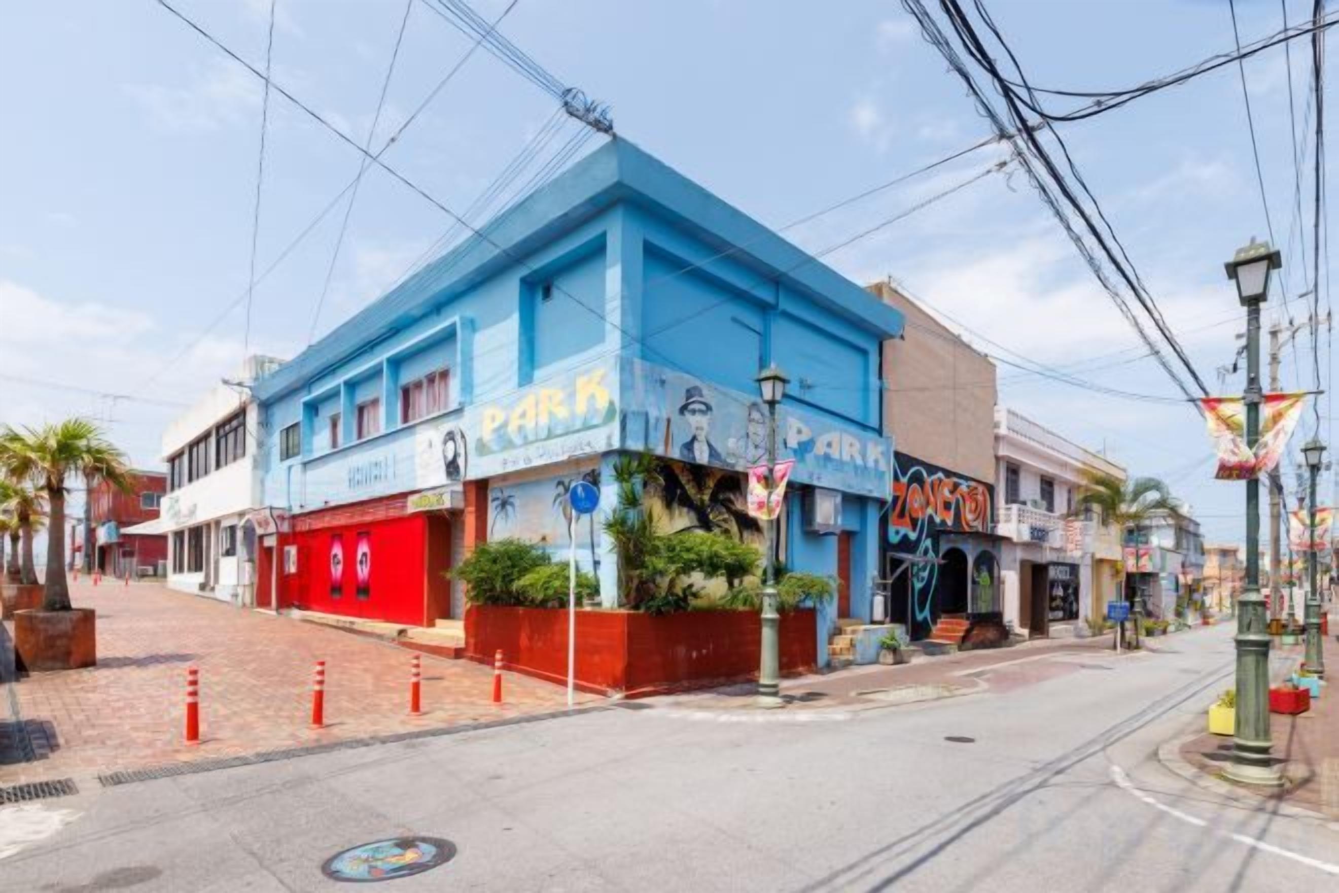 A street view with a blue building with a 'Park' sign, a red awning, and a sidewalk with orange traffic cones.