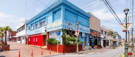 A street view with a blue building with a 'Park' sign, a red awning, and a sidewalk with orange traffic cones.