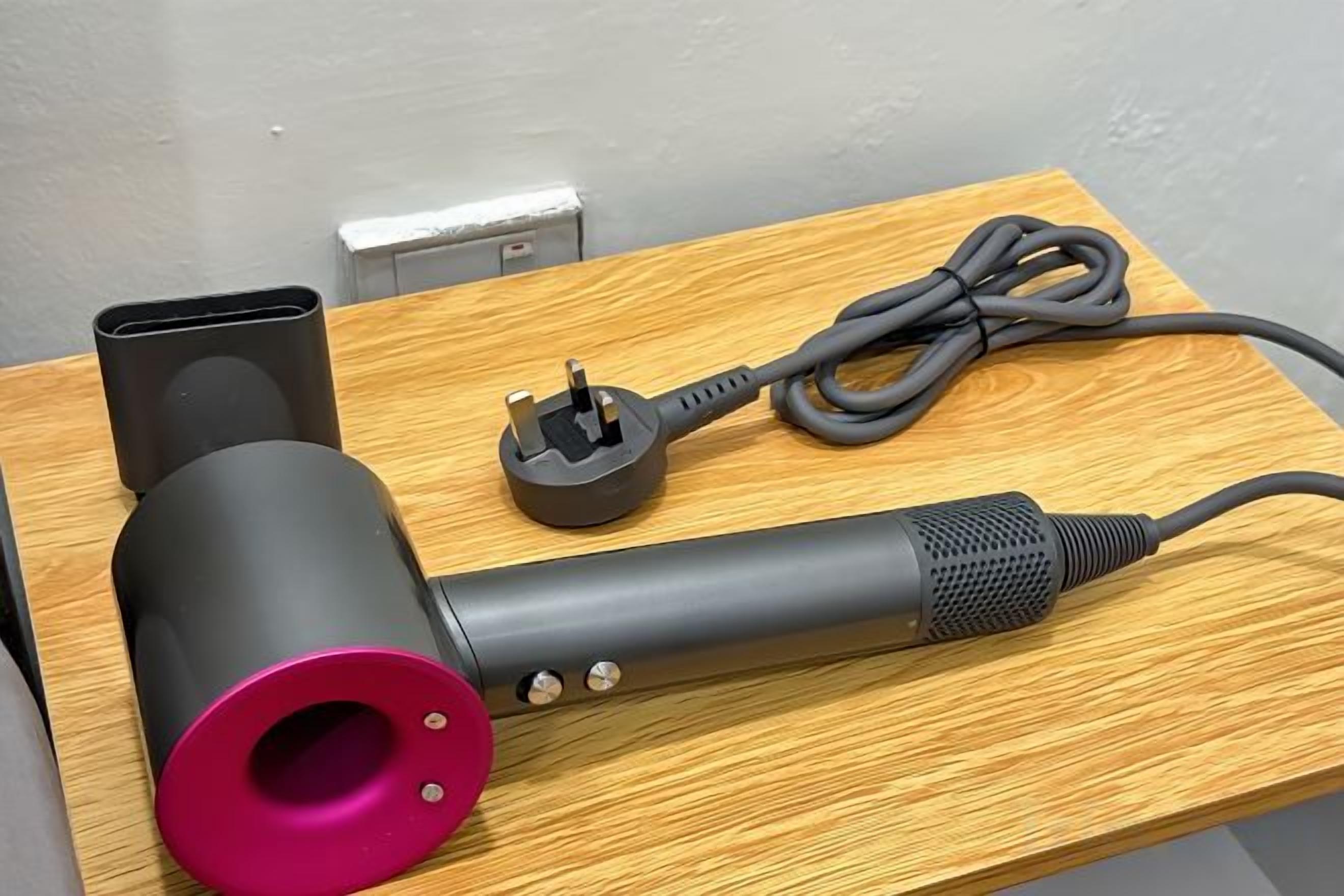 Un appareil cylindrique avec un couvercle rose et un cordon noir, posé sur une surface en bois.