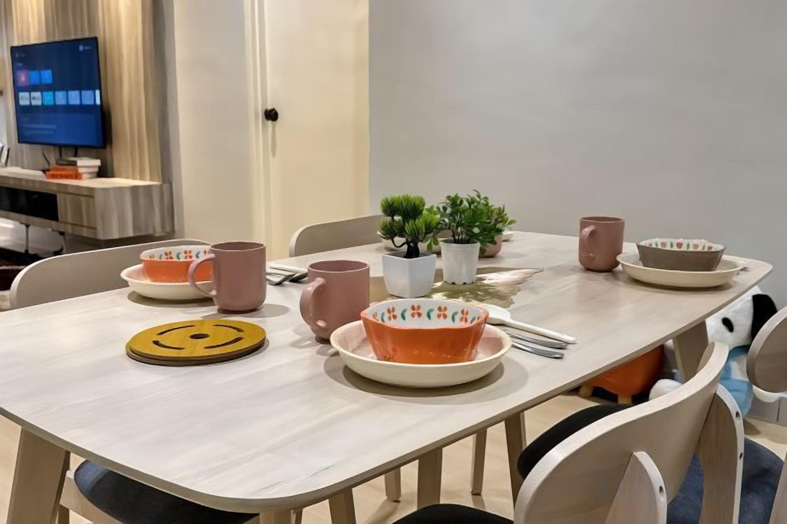 A dining table with plates, bowls, and mugs, a small plant, and a smiley face coaster.