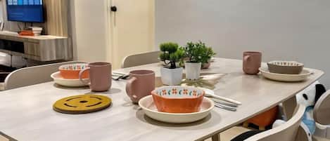 A dining table with plates, bowls, and mugs, a small plant, and a smiley face coaster.