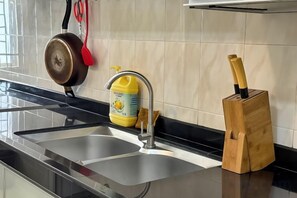 Une cuisine avec un évier en acier inoxydable, un produit de nettoyage jaune et un bloc à couteaux en bois.