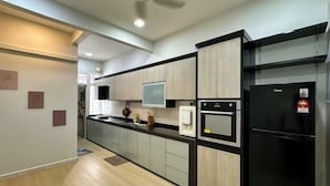 A modern kitchen with light wood cabinets, a black refrigerator, and a built-in oven. - Austin Landed Honey Nest 10pax (Tebrau)
