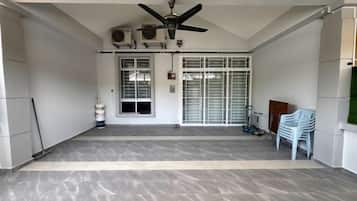 A covered outdoor area with a ceiling fan, air conditioning units, a door with a window, and a white plastic chair.
