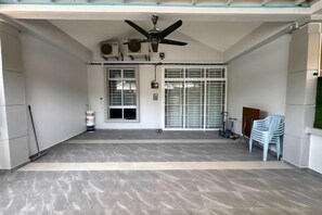 A covered outdoor area with a ceiling fan, air conditioning units, a door with a window, and a white plastic chair.