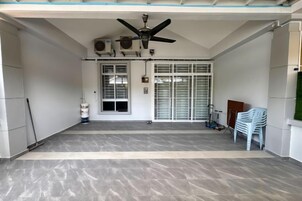 A covered outdoor area with a ceiling fan, air conditioning units, a door with a window, and a white plastic chair.