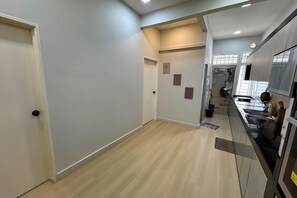 A hallway with a door on the left, a kitchen area with a sink and cabinets on the right, and a small rug on the floor.