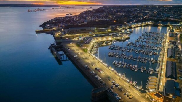 An aerial view of a marina with boats docked, a bridge, and a town in the background during sunset. - The Penthouse - 1 Bedroom Penthouse - Milford Haven (Milford Haven)