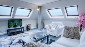 A modern living room with a flat-screen TV, white furniture, and skylights.