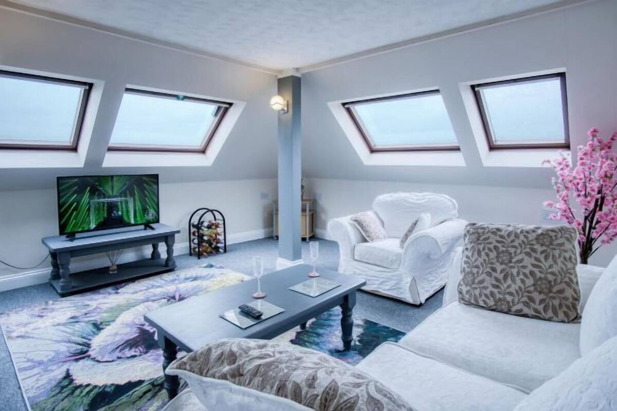 Ein modernes Wohnzimmer mit Flachbildfernseher, einem weißen Sofa, einem Couchtisch und einem großen Fenster.