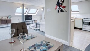 A modern apartment with a dining area, a kitchen, and a living room with a TV and seating. - The Penthouse - 1 Bedroom Penthouse - Milford Haven (Milford Haven)