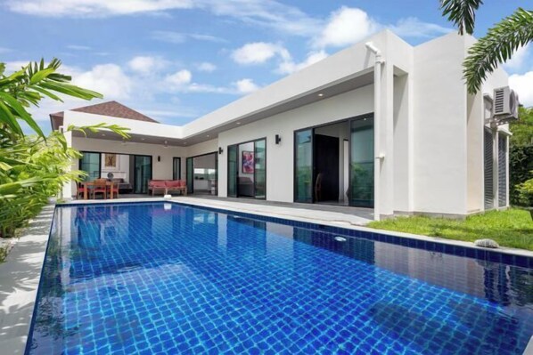 Una moderna casa con piscina, ampie vetrate e facciata bianca.