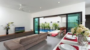 Un salon moderne avec un canapé, une table à manger dressée avec des assiettes et un vase de fleurs, et un téléviseur posé sur un meuble.