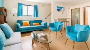 A modern living room with a teal sofa, matching armchairs, a glass coffee table, and a staircase leading to a dining area. - Senju gawaracho 2･3F (Tokyo)