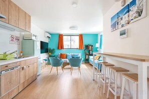 A modern kitchen with wooden cabinets, a dining area with blue chairs, and a kitchen island with stools. - Senju gawaracho 2･3F (Tokyo)