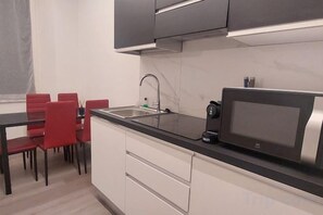 Een moderne keuken met een zwart aanrecht, een magnetron en een spoelbak. Er staan rode stoelen rond een eettafel.