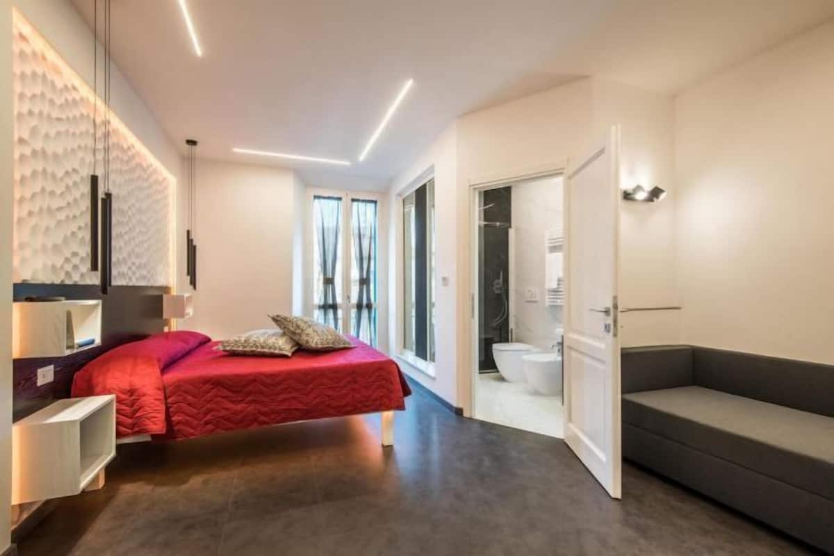 A modern bedroom with a bed, bedside tables, a built-in wardrobe, and a bathroom with a toilet and shower.