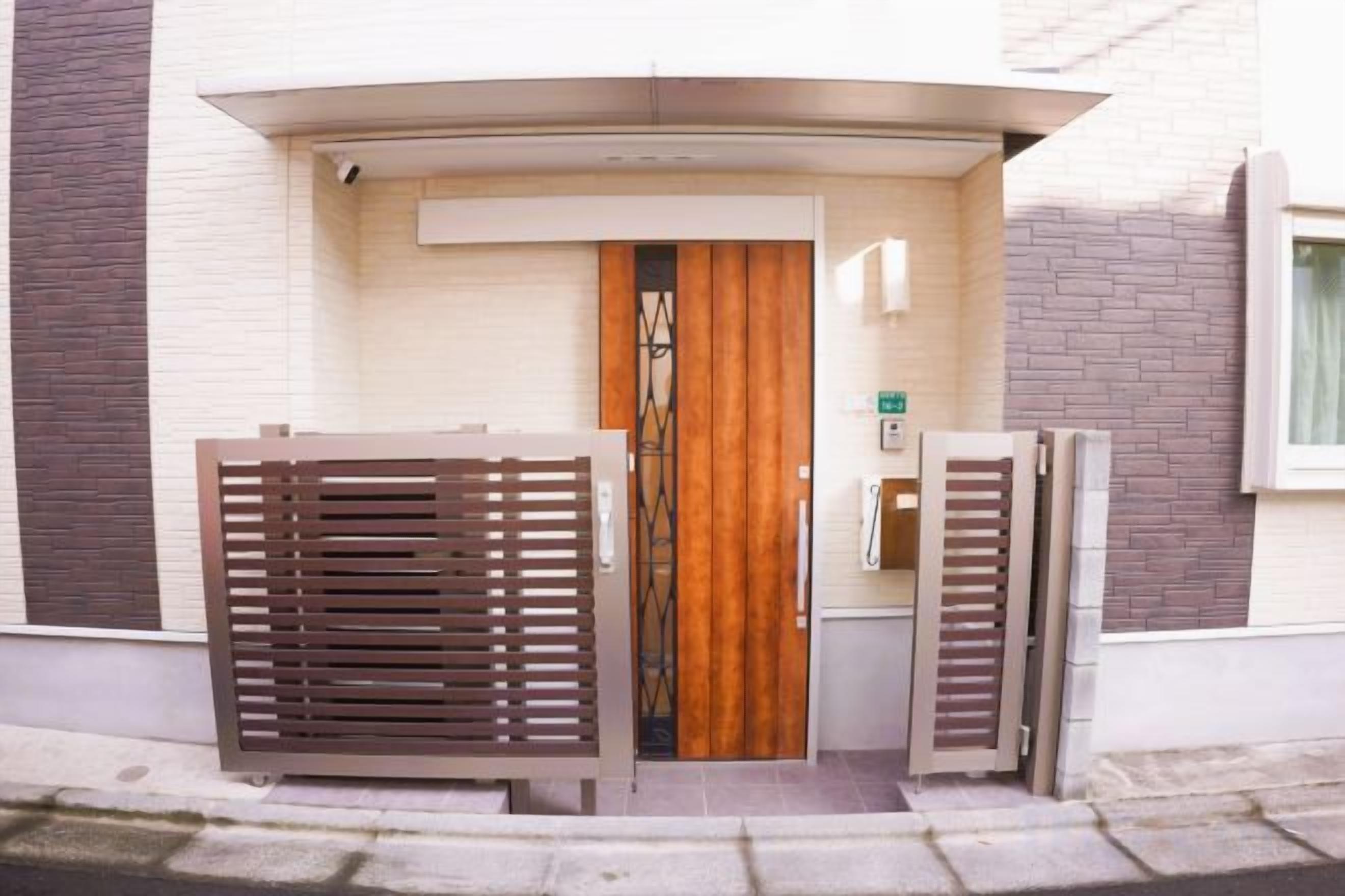 Une entrée d’immeuble avec une porte en bois, un portail en métal et une petite fenêtre sur la droite.