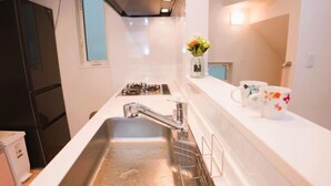 A kitchen with a stainless steel sink, a stove, and a countertop with a vase of flowers and a mug. - Tokyo　Ikebukuro　villa (Tokyo)