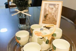 Une table mise avec une théière, des tasses, un vase avec une plante et un tableau encadré.