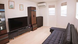 A living room with a flat-screen TV, dark-colored furniture, and an air conditioning unit. - Tokyo　Ikebukuro　villa (Tokyo)