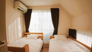 A small, well-lit room with two single beds, a window with curtains, and an air conditioning unit. - Tokyo　Ikebukuro　villa (Tokyo)