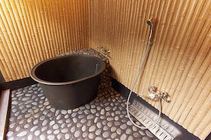 A spa room with a stone-tiled floor, a black bathtub, and a bamboo wall. - KYOBU Karasuma Gojo (Kyoto)