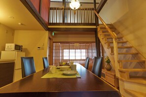 A dining area with a wooden table, chairs, a microwave, and a staircase. - KYOBU Karasuma Gojo (Kyoto)